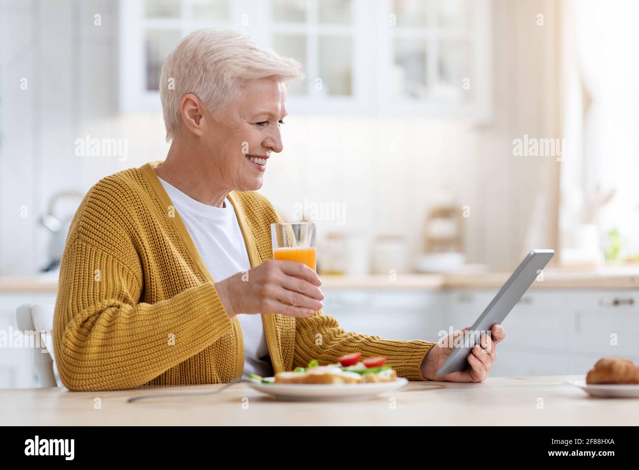 Dame aînée joyeuse avec tablette numérique pour déjeuner, vue latérale Banque D'Images