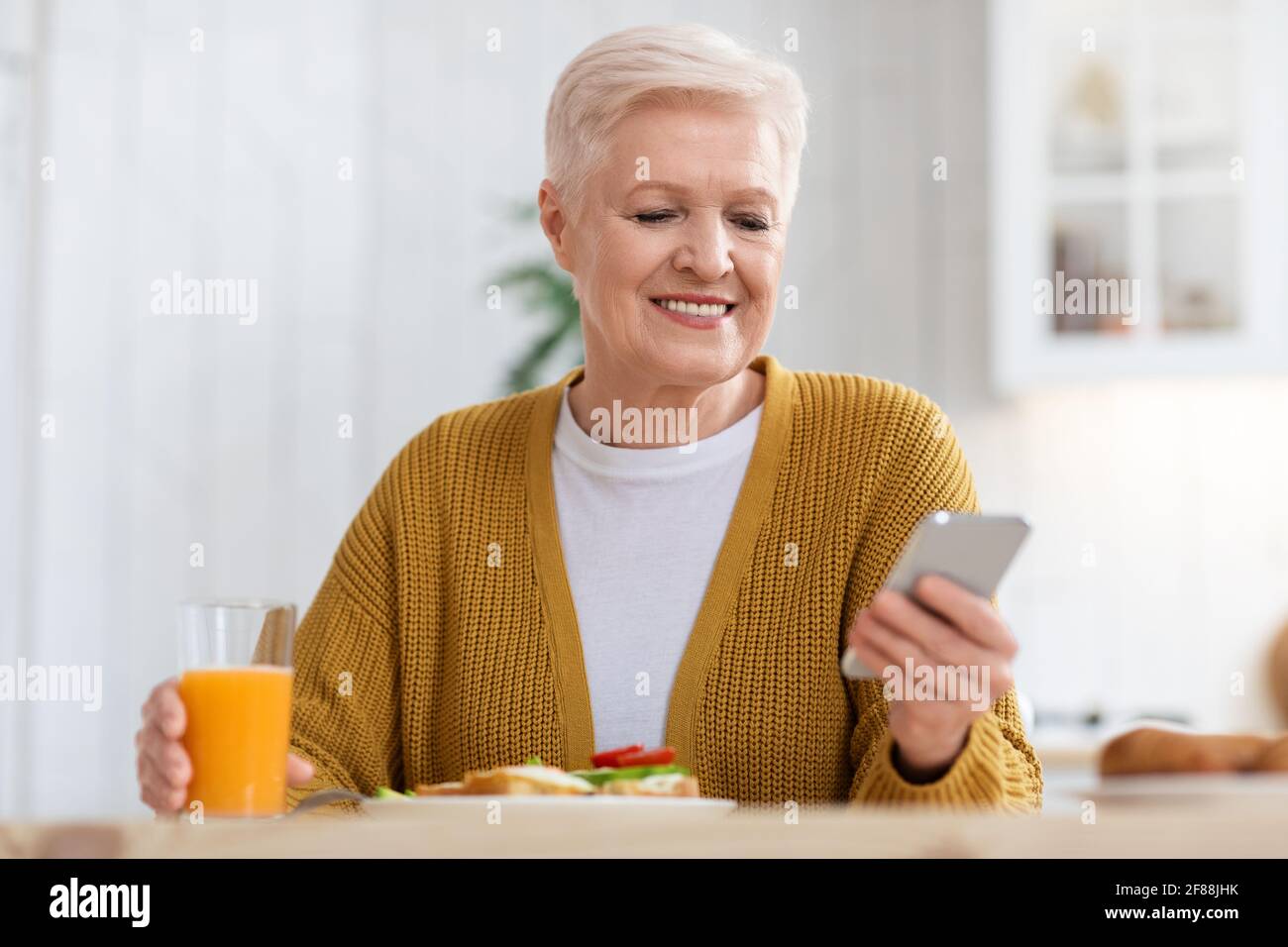 Femme âgée souriante utilisant un téléphone portable tout en déjeunant, en gros plan Banque D'Images