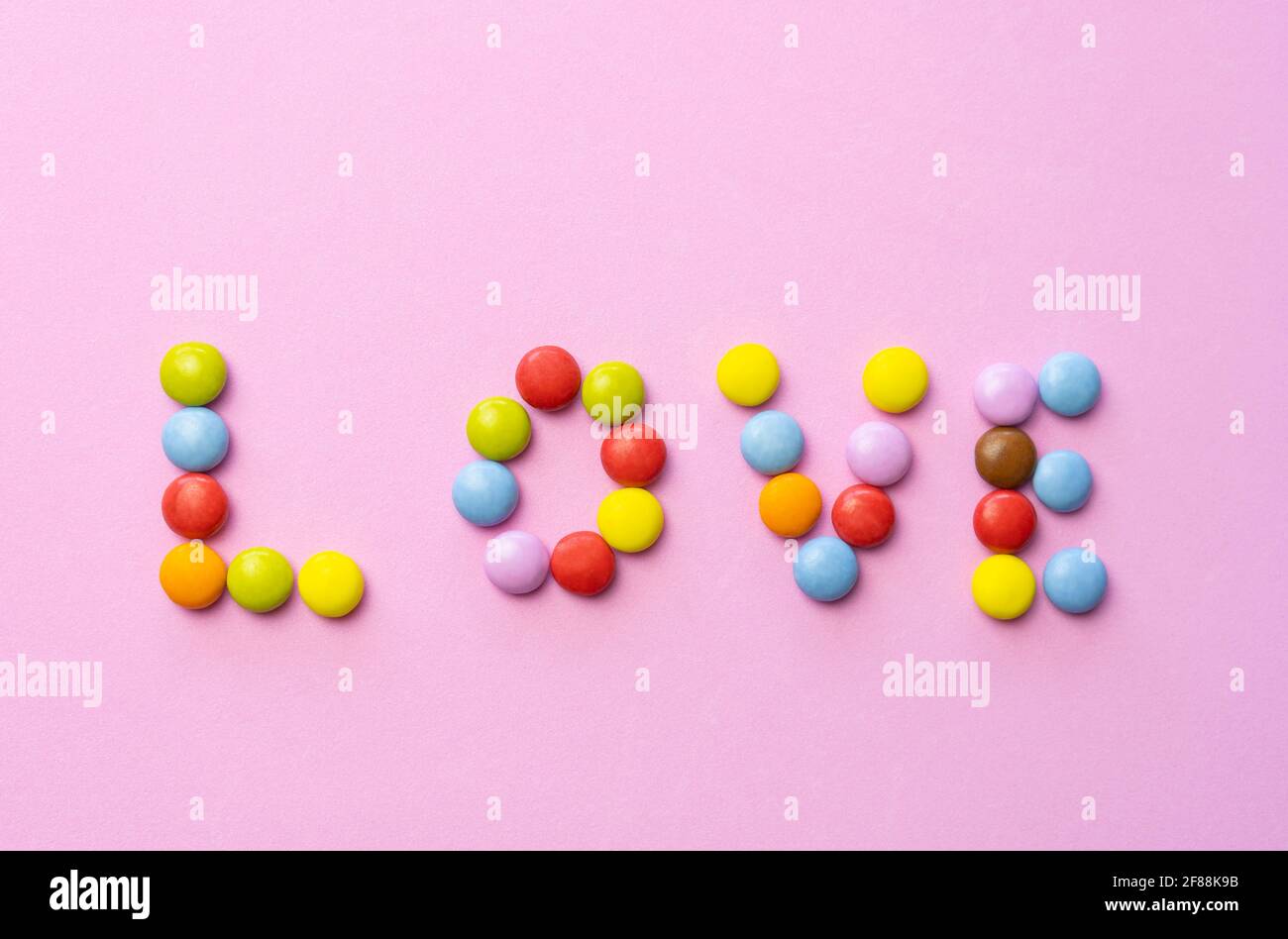 Le mot AMOUR fait à partir de chocolat coloré de bonbons intelligents sur fond rose.multicolore amour fond de nourriture. Banque D'Images