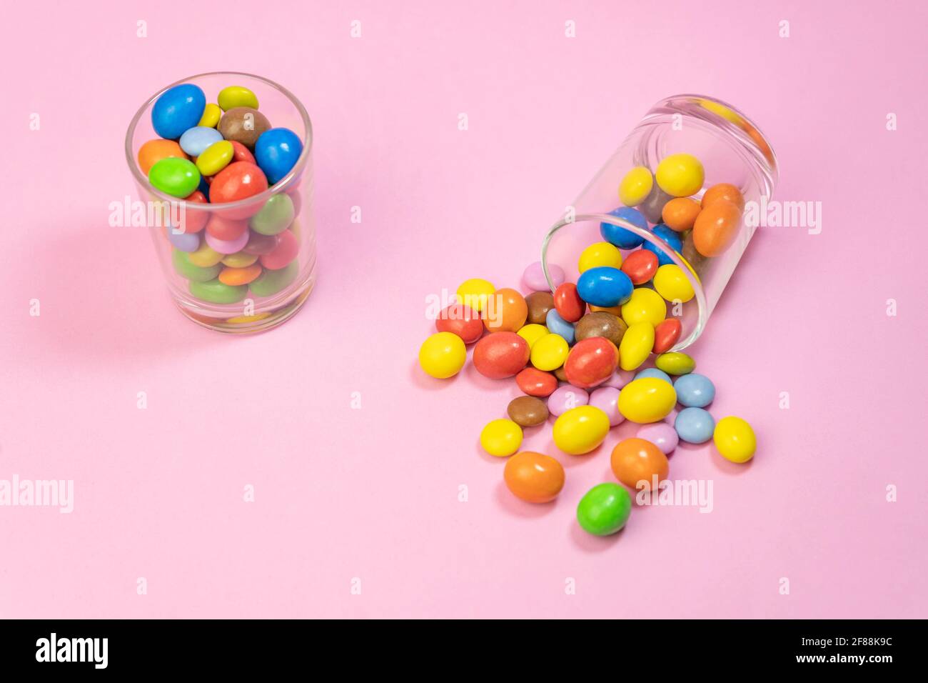 Bonbons au chocolat multicolores éparpillés dans deux verres sur fond rose.Haut vue sur le concept d'arrière-plan des bonbons créatifs et colorés avec espace de copie pour t Banque D'Images