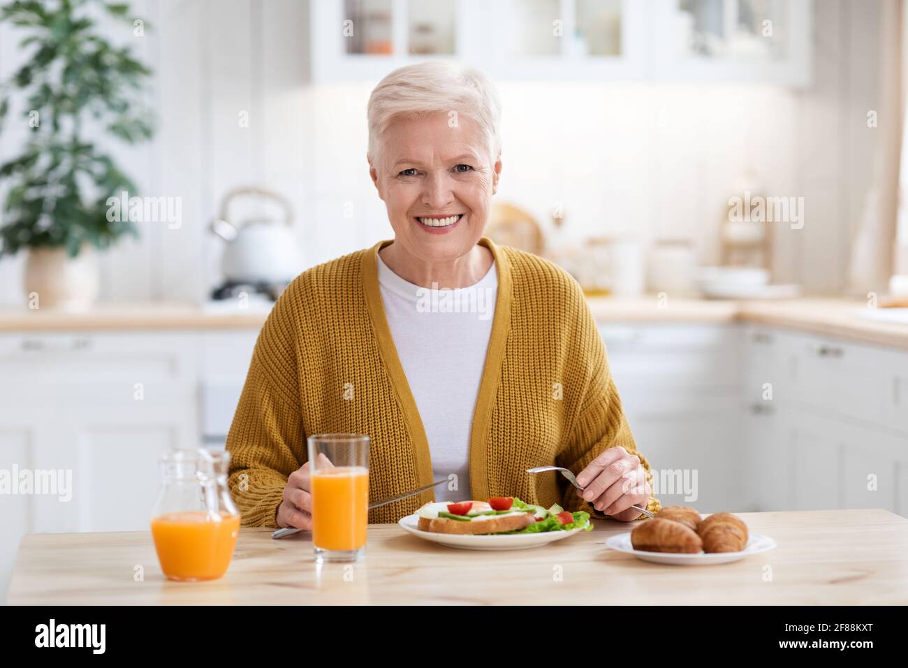 Grand-mère attrayante ayant déjeuner dans la cuisine seule Banque D'Images
