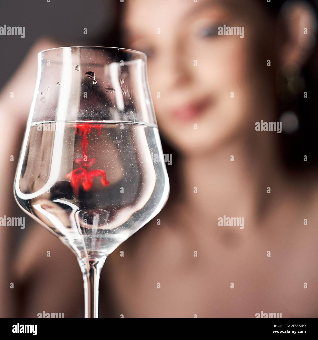 Gouttes de peinture rouge dans un verre d'eau, une femme regarde le verre. Banque D'Images