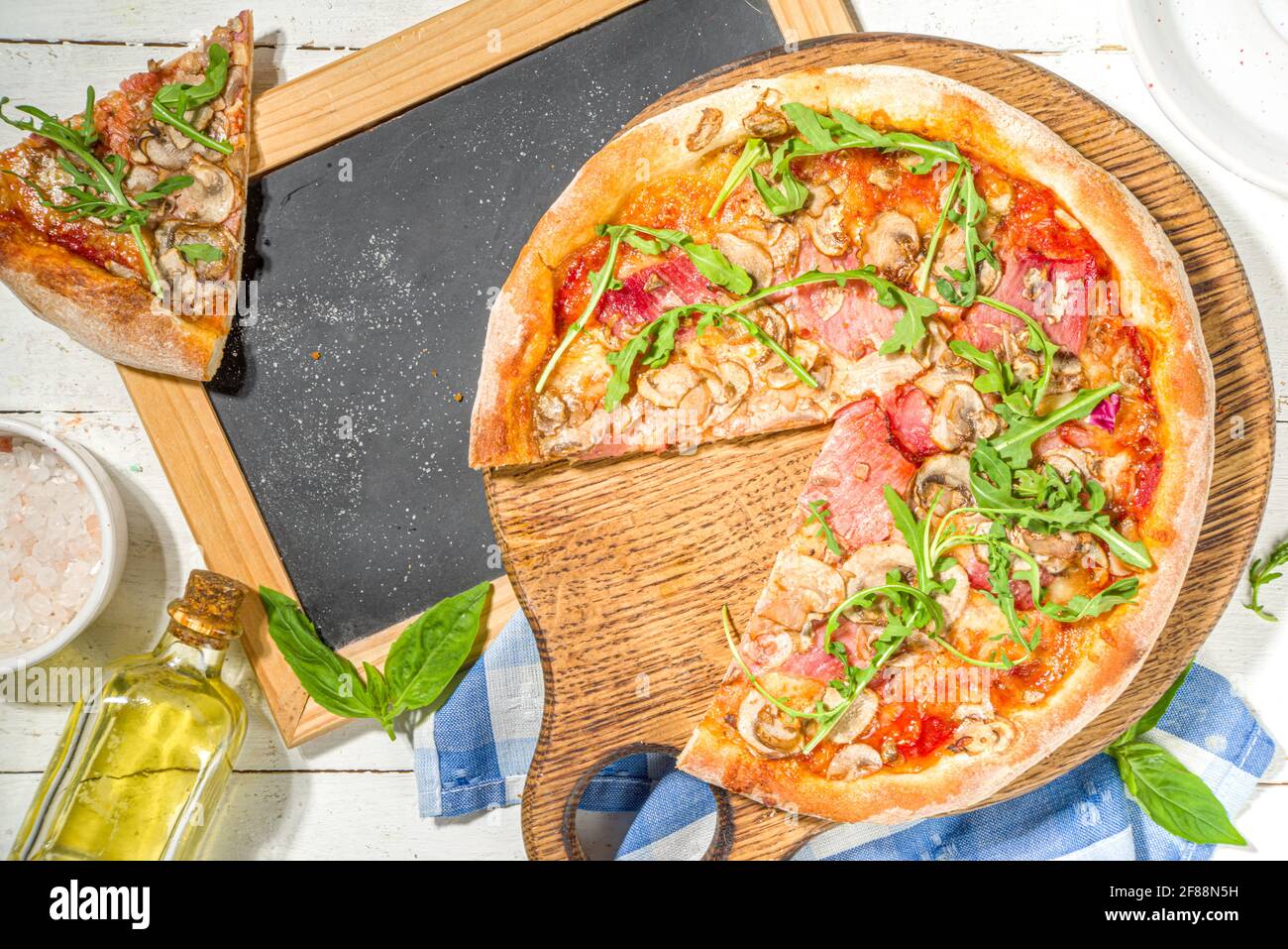 Savoureuse pizza traditionnelle italienne avec jambon et champignons, sur fond de bois blanc. Concept de recette de cuisine méditerranéenne, vue de dessus Banque D'Images