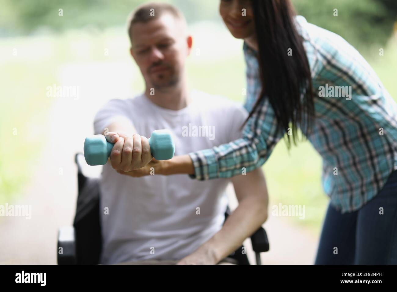 Infirmière aidant le jeune homme handicapé en fauteuil roulant à lever l'haltère gros plan Banque D'Images