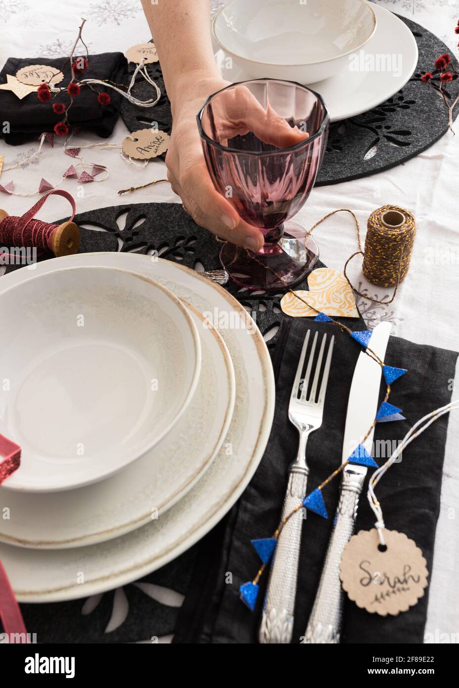 Un joli verre violet transparent est tenu par un homme main dans une table de fête de Noël ornée. Certains noms flous sont sur des balises rondes tout autour de TH Banque D'Images