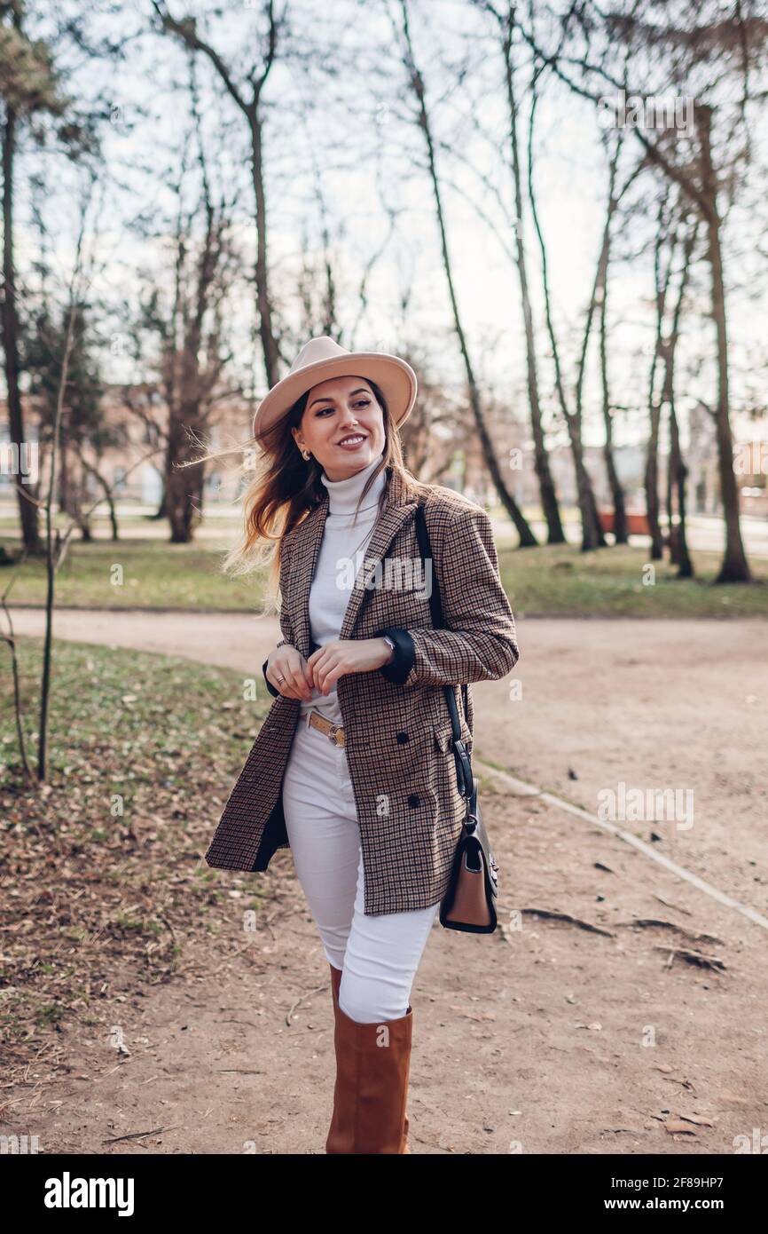 Belle jeune femme portant un blazer, un chapeau et des bottes élégants  tenant un sac à main dans le parc. Tenue tendance printemps femme coloris  blanc et marron Photo Stock - Alamy