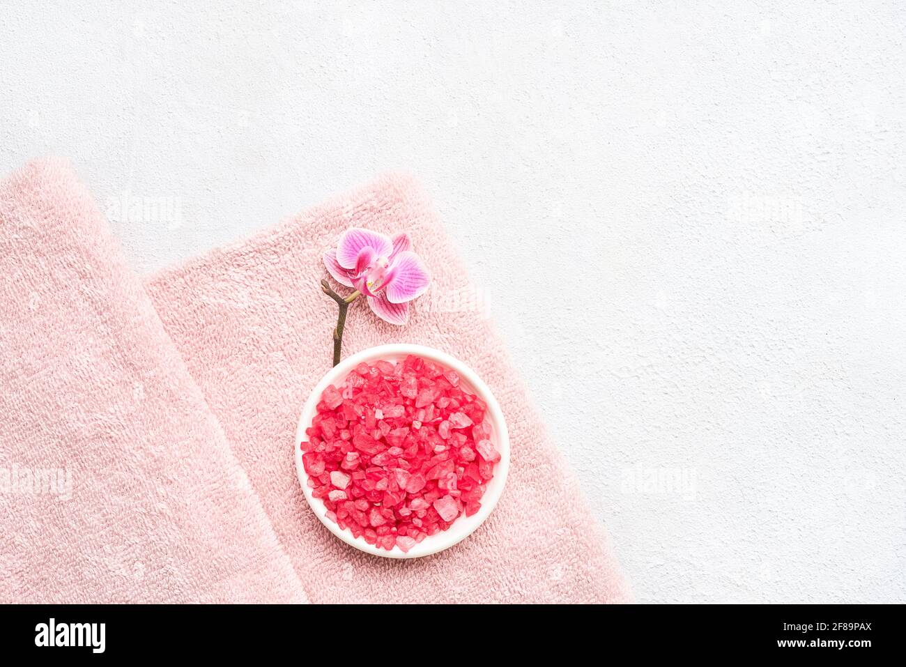 Serviettes roses pliées, sel de bain rose et fleur d'orchidées sur fond blanc en béton. SPA, hygiène, bien-être, concept de soins du corps. Espace de copie, Banque D'Images