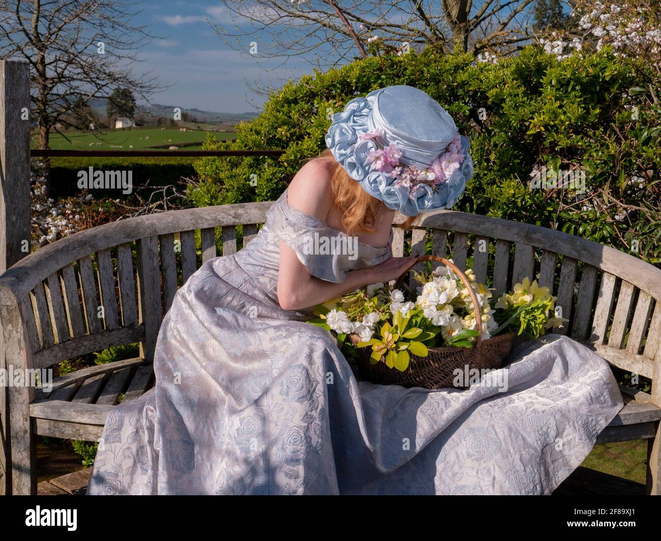 Jeune femme dans un bonnet de Pâques et dans l'épaule de longues dragues  assis sur le banc de la plate-forme de visualisation et pencher sur le  panier à fleurs Photo Stock -