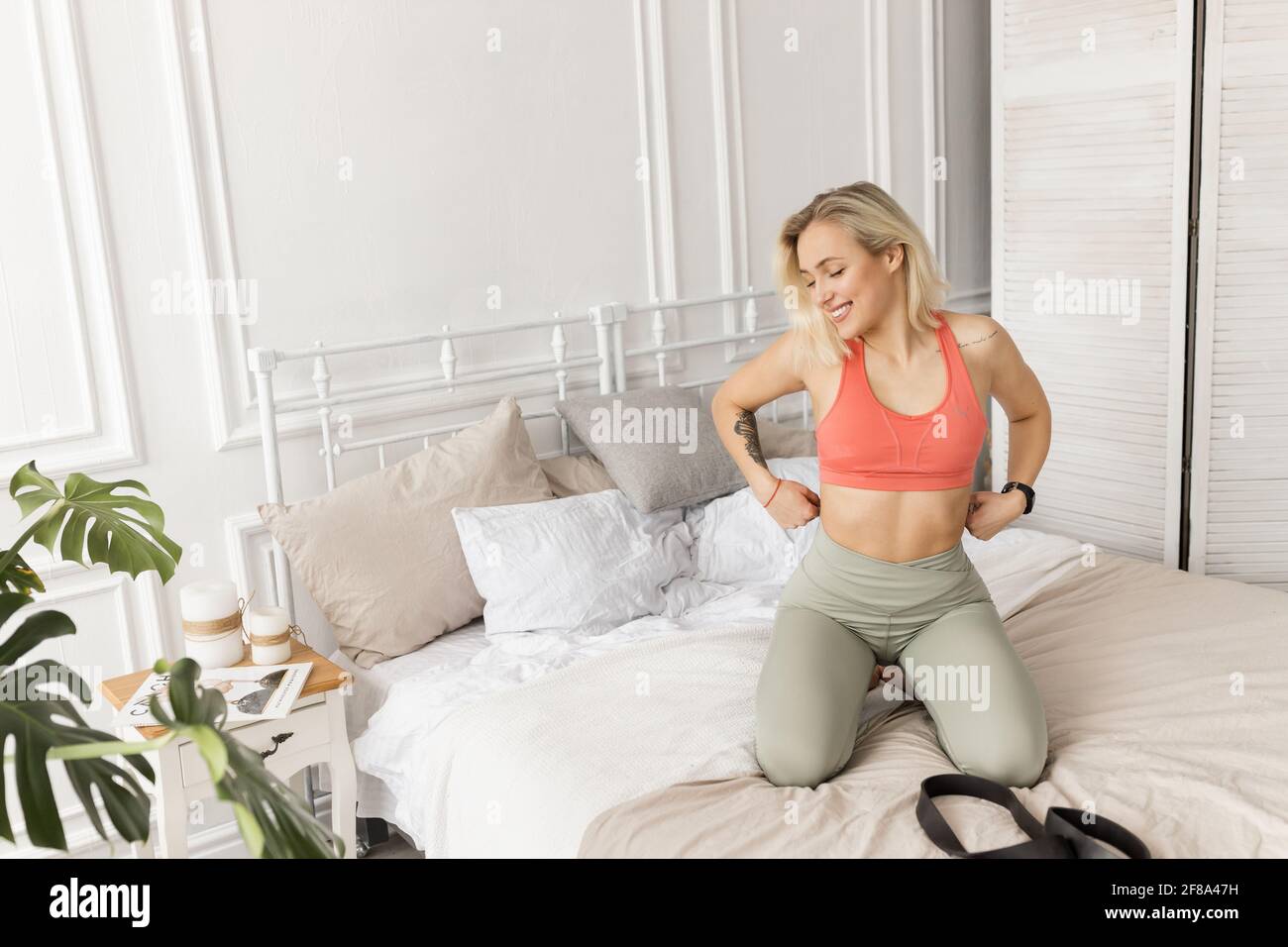 Femme sportive de bonne humeur se prépare à faire de l'exercice le matin,  assise sur un lit. Belle femme se préparant à faire des exercices avec une  bande élastique Photo Stock -