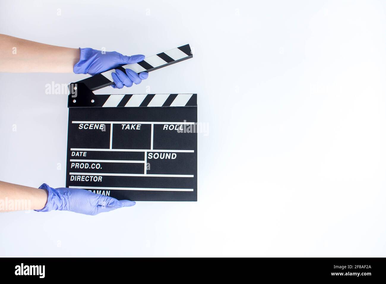 Femme en caoutchouc bleu jetable gants tenant le film clapper. Influence de la pandémie sur le cinéma Banque D'Images