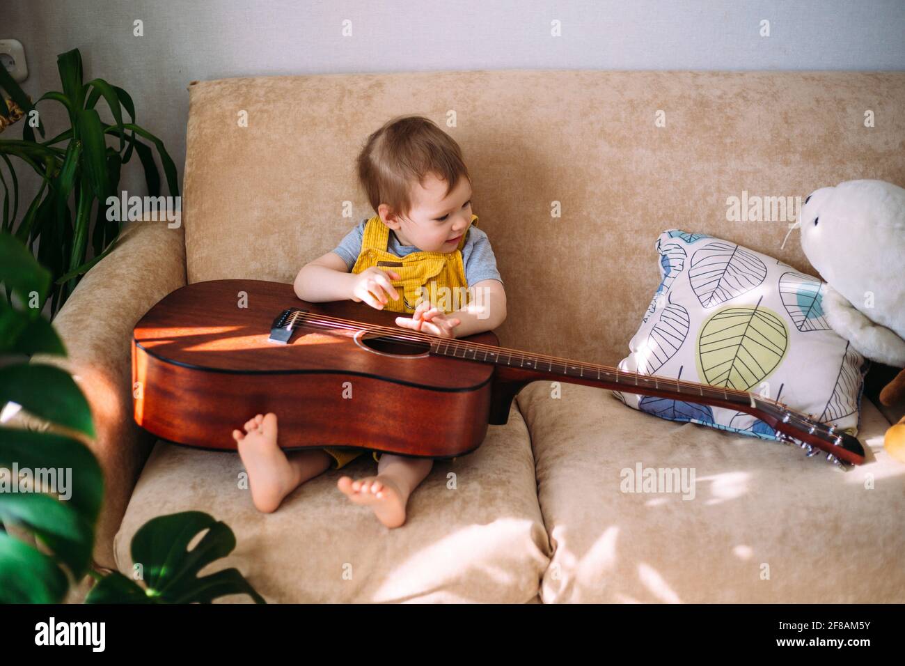 Un enfant mignon joue avec une grosse guitare acoustique à à la maison sur le canapé Banque D'Images