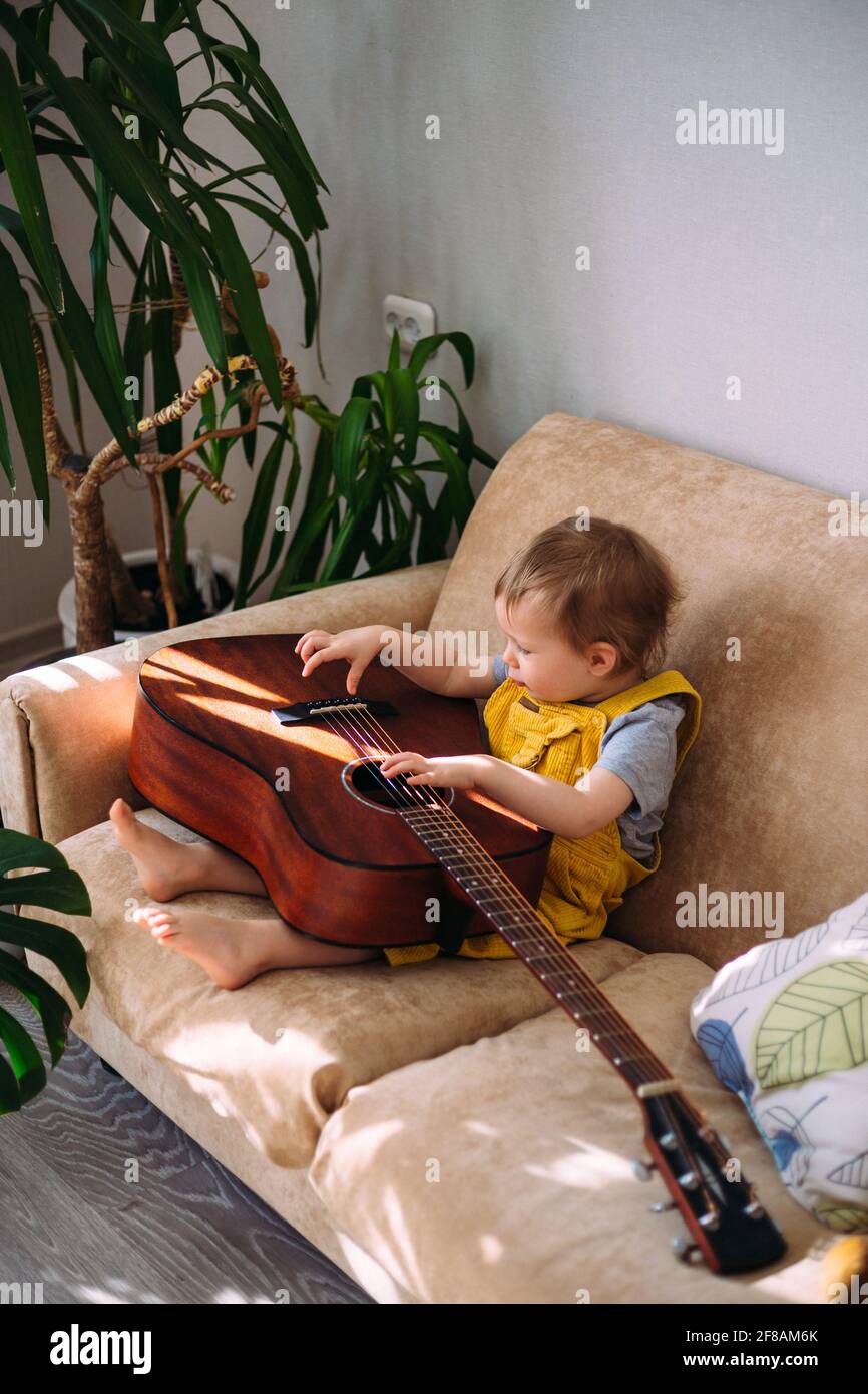 Un enfant mignon joue avec une grosse guitare acoustique à à la maison sur le canapé Banque D'Images