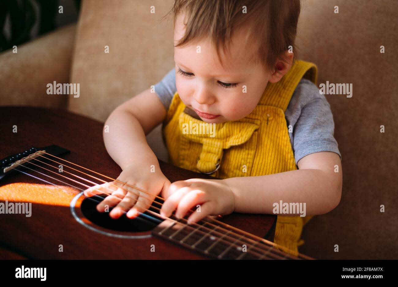 Un enfant mignon joue avec une grosse guitare acoustique à à la maison sur le canapé Banque D'Images