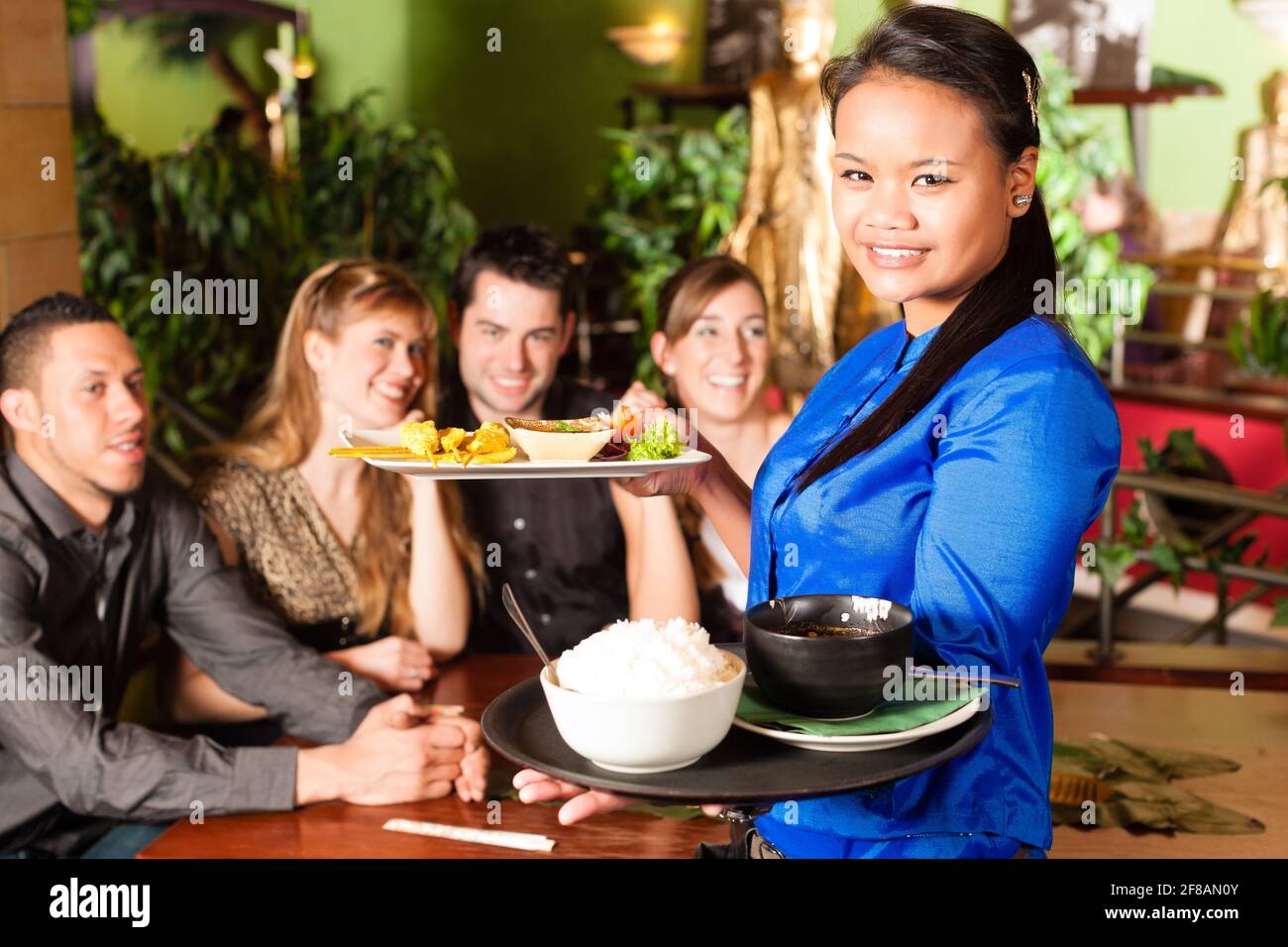 Les jeunes de manger dans un restaurant thaïlandais, la serveuse apporte les plats, le riz et d'autres Banque D'Images