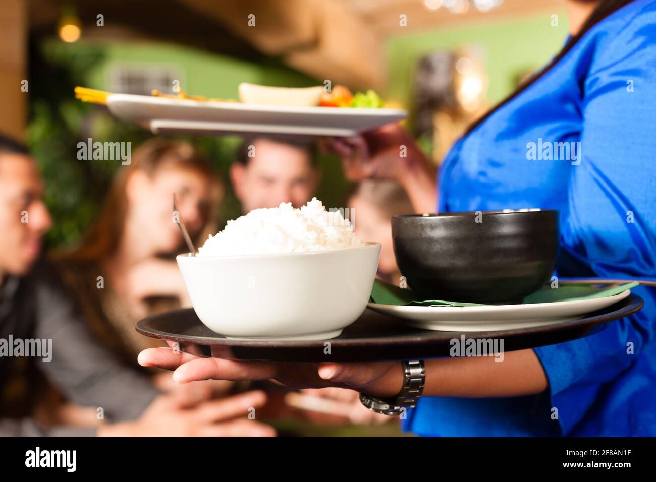 Les jeunes de manger dans un restaurant thaïlandais, la serveuse apporte les plats, le riz et d'autres Banque D'Images