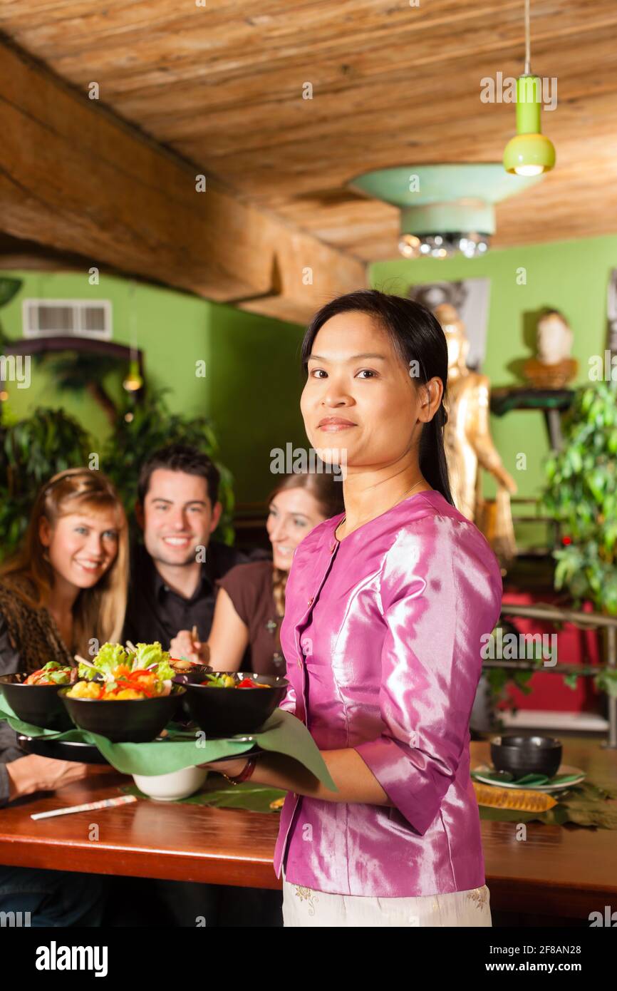 Les jeunes de manger dans un restaurant thaïlandais, la serveuse apporte les plats, le riz et d'autres Banque D'Images