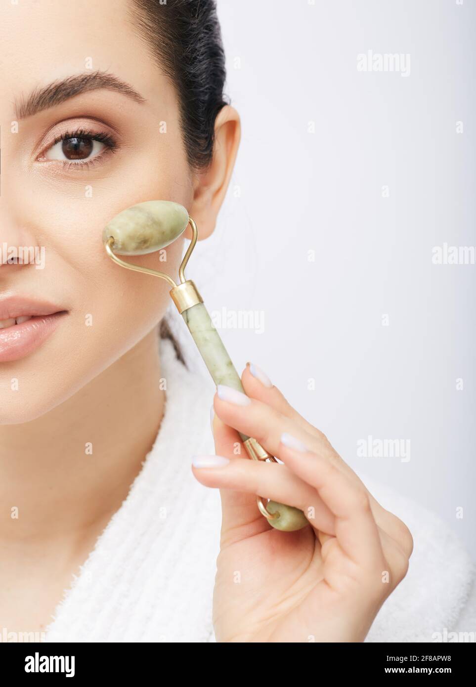 Faites face au rouleau de jade. Demi-visage d'une femme hispanique avec jade ou rouleau de pierre pour la procédure anti-âge Banque D'Images