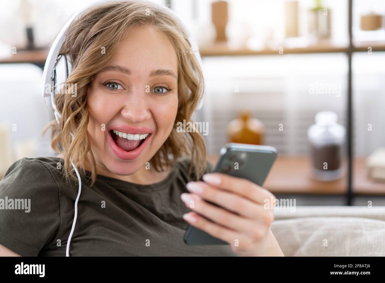 Des dents heureuses sourient femme écouter de la musique casque tenant le smartphone dans Main caucasienne femme appréciez balado ou livres audio tout en restin sur la table, fermer u Banque D'Images