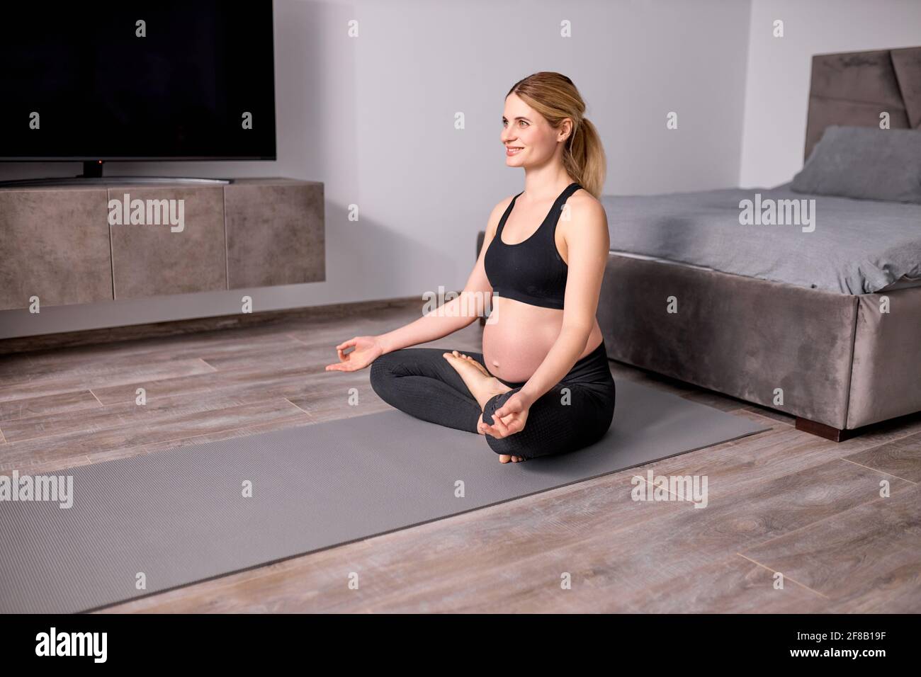 Femme enceinte agréable méditant sur le sol à la maison, avec des jambes croisées, dans le Black Sportswear, Namaste, garder le calme. Vue latérale Banque D'Images