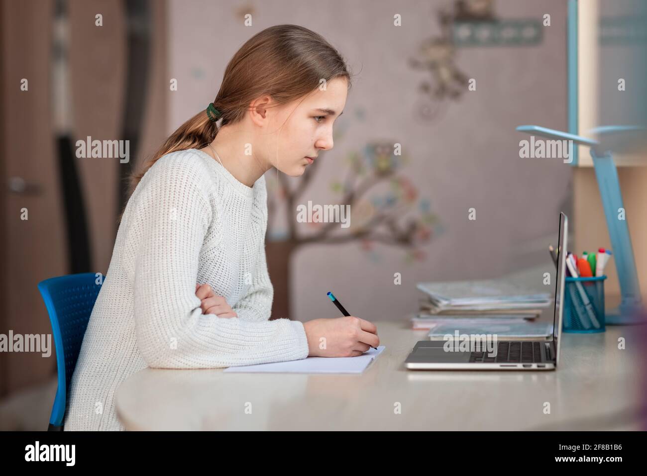 Belle fille d'école souriante étudiant à la maison faisant des devoirs à l'école. Livres de formation et carnet sur la table. Enseignement en ligne à distance Banque D'Images
