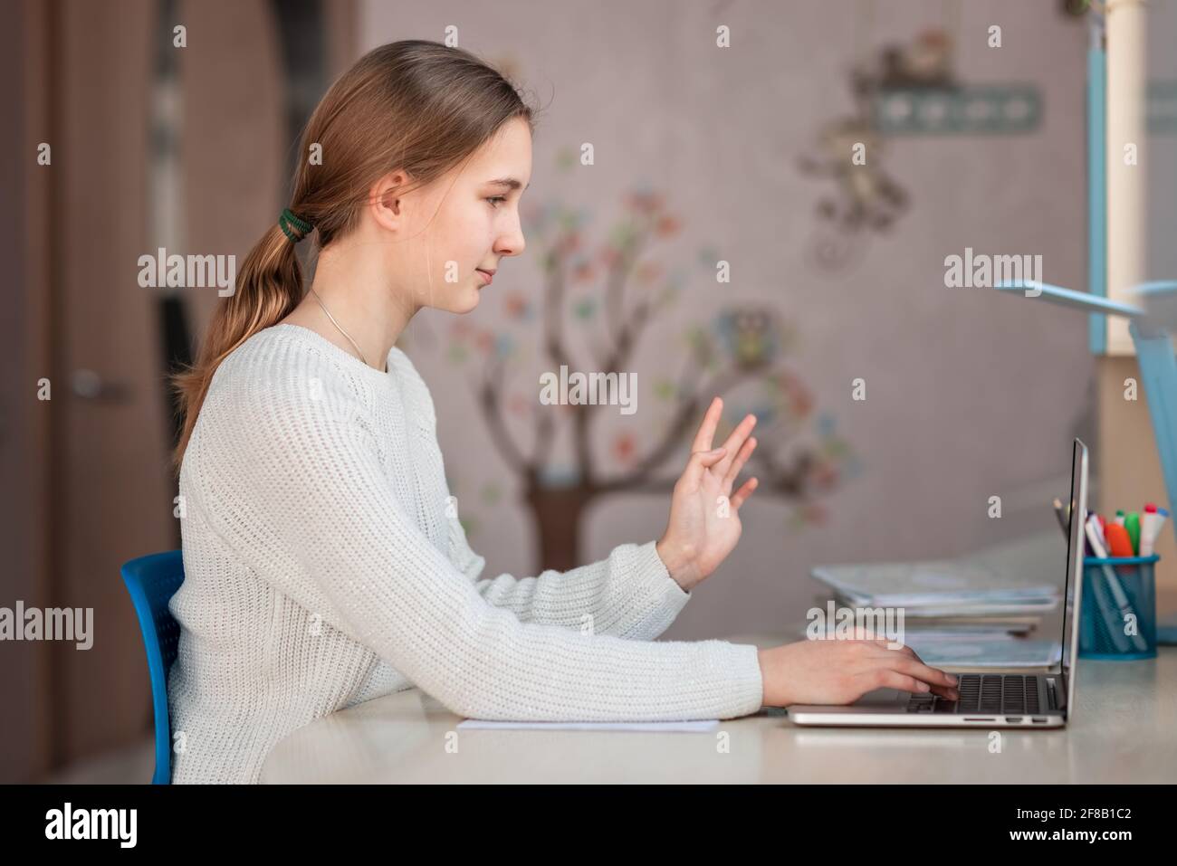 Belle fille d'école souriante étudiant à la maison faisant des devoirs à l'école. Livres de formation et carnet sur la table. Enseignement en ligne à distance Banque D'Images
