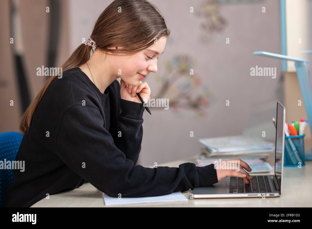 Belle fille d'école souriante étudiant à la maison faisant des devoirs à l'école. Livres de formation et carnet sur la table. Enseignement en ligne à distance Banque D'Images