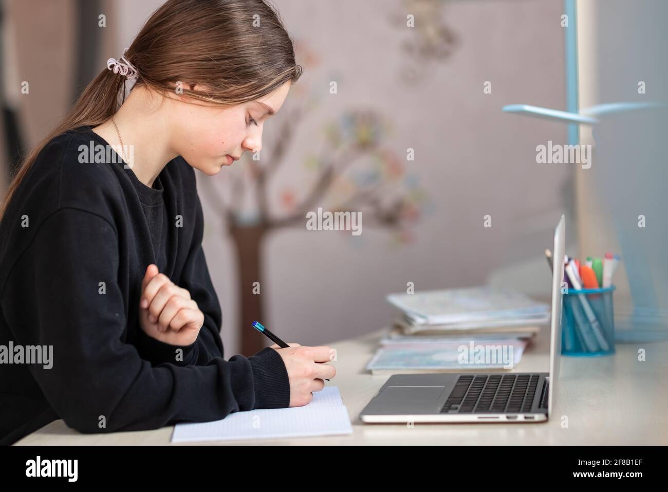 Belle fille d'école souriante étudiant à la maison faisant des devoirs à l'école. Livres de formation et carnet sur la table. Enseignement en ligne à distance Banque D'Images