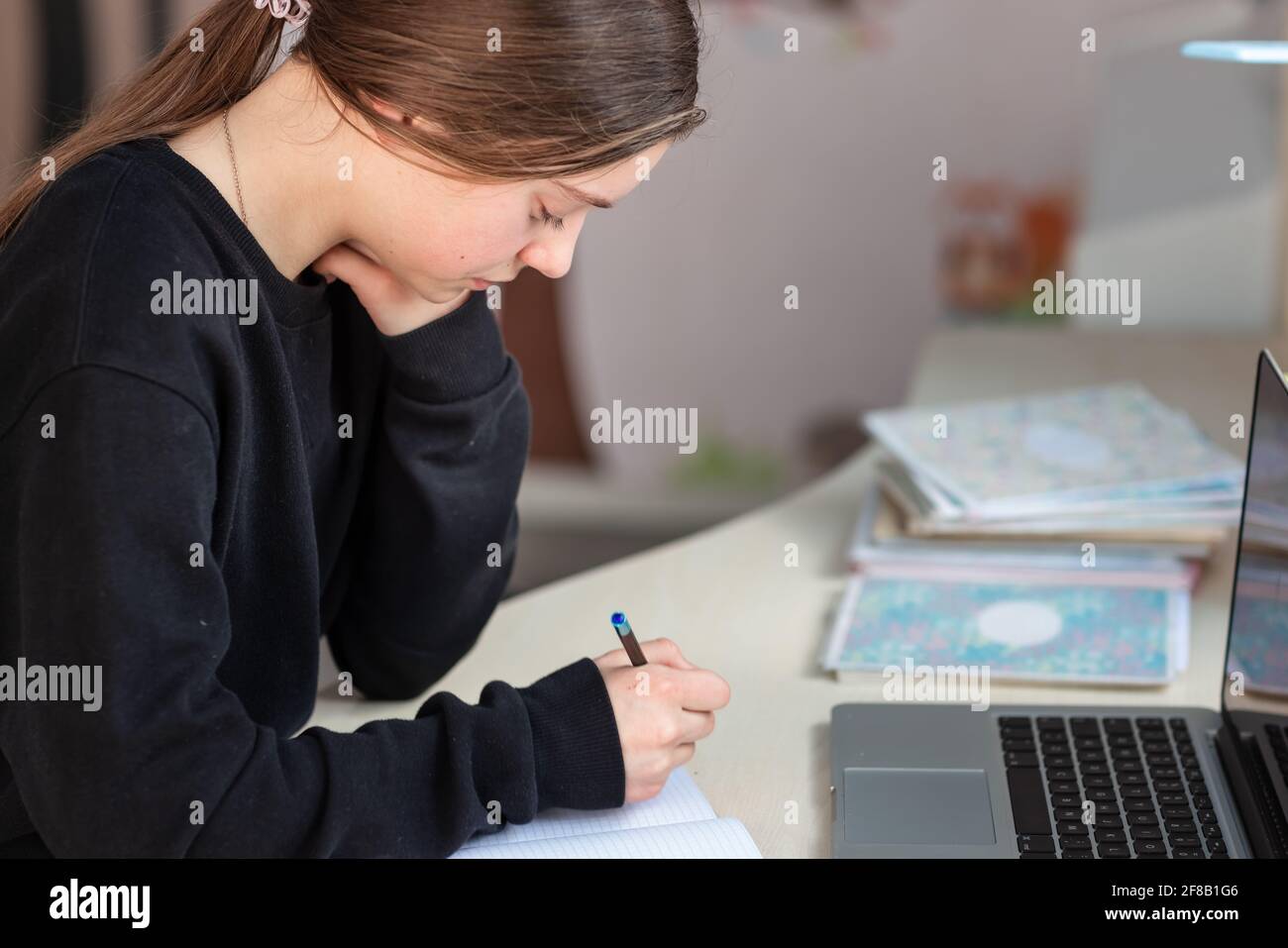 Belle fille d'école souriante étudiant à la maison faisant des devoirs à l'école. Livres de formation et carnet sur la table. Enseignement en ligne à distance Banque D'Images