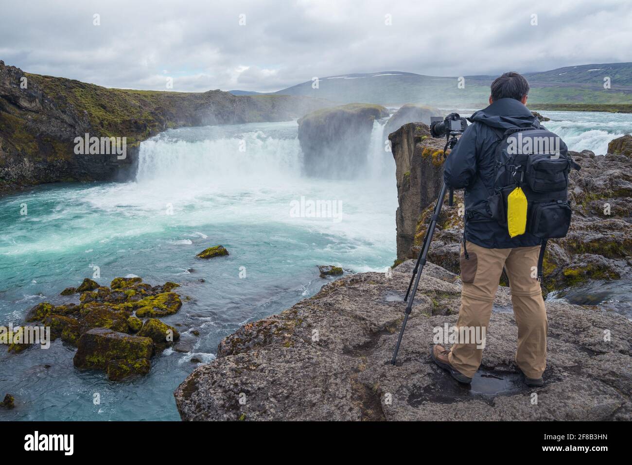 Photographe avec sac à dos et trépied surplombant la cascade islandaise Godafoss lors d'une journée nuageux. Banque D'Images