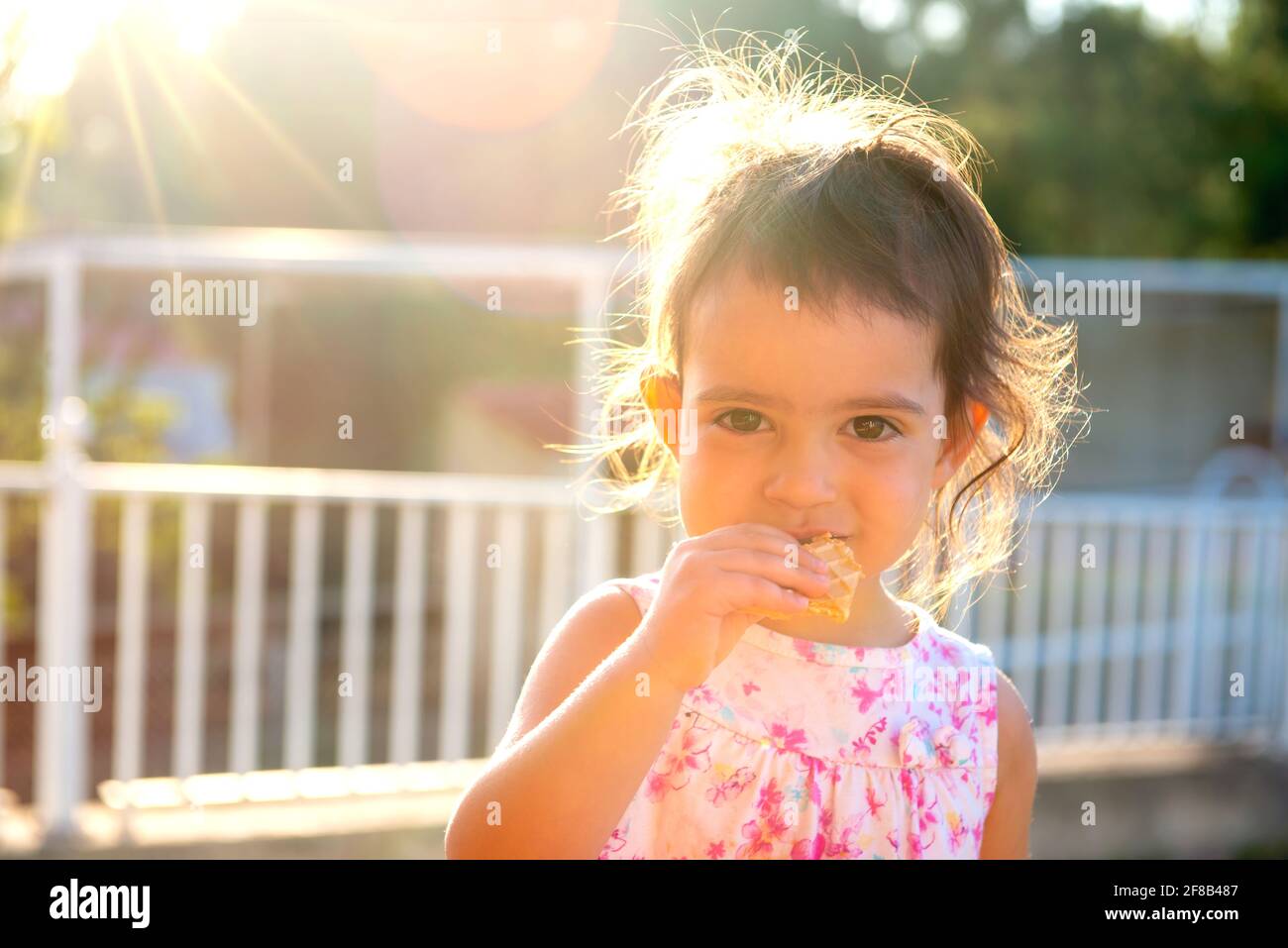 Douce jeune fille mangeant un cookie à l'extérieur au coucher du soleil Banque D'Images