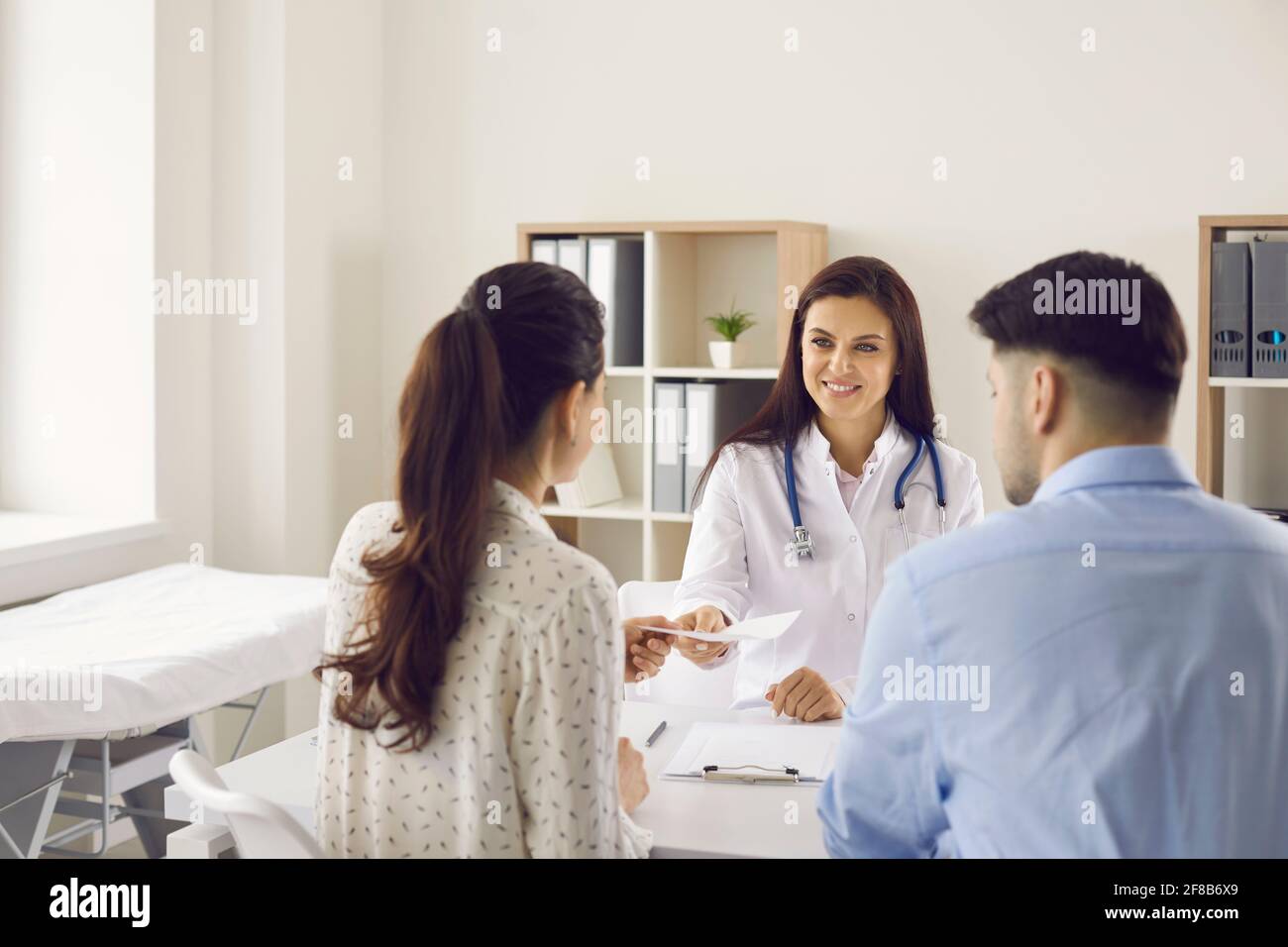 Le médecin donne une référence pour un examen médical d'un couple assis avec leur dos à la caméra Banque D'Images