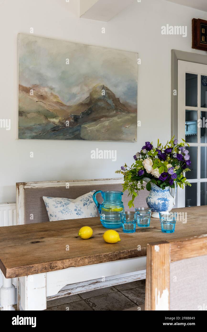 Œuvre de Sue Green au-dessus de la table avec des bancs Gustavian dans West Sussex cuisine repensée. Banque D'Images