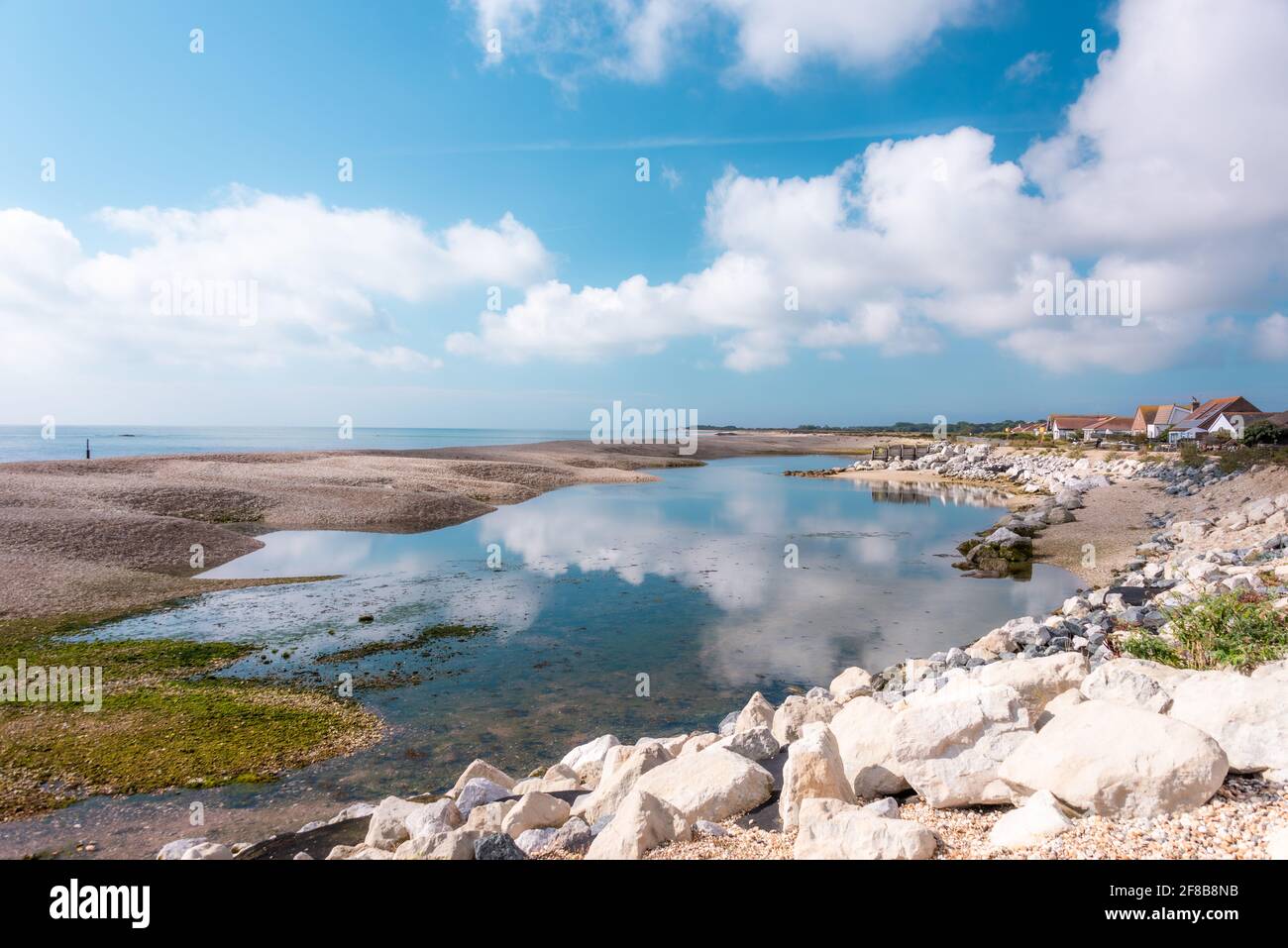 Maisons côtières avec nuages reflétés à Pagham, West Sussex. Banque D'Images