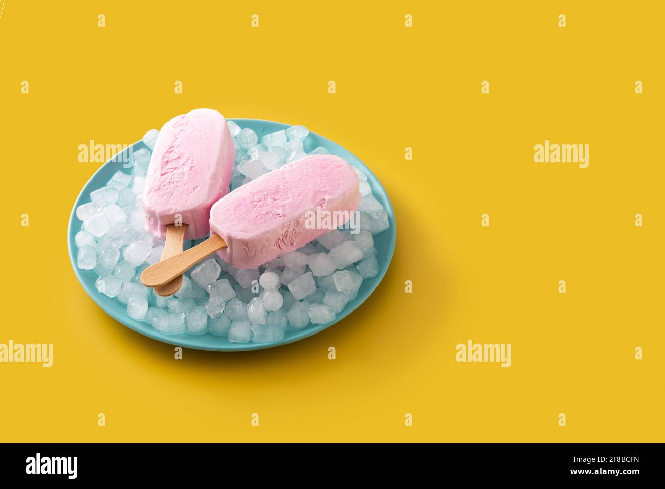 Des pop-glaces aux fraises et de la glace pilée sur une assiette bleue sur du jaune arrière-plan Banque D'Images