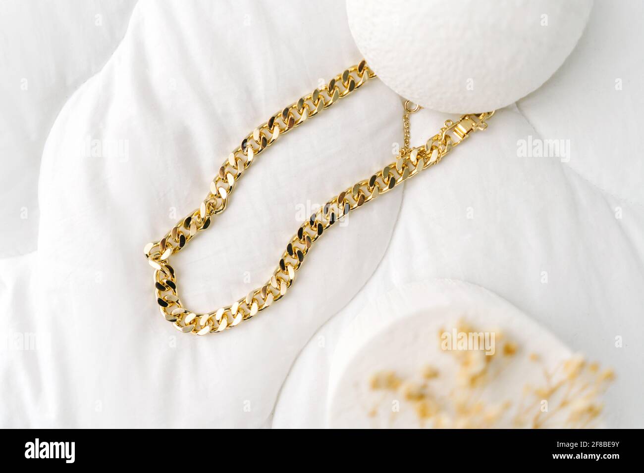 Bijoux imitation, chaîne de bijoux en or sur fond textile blanc. Sécher les petites fleurs comme la décoration. Banque D'Images