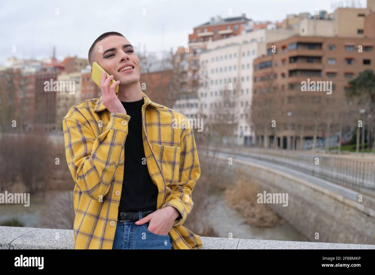 Jeune personne non binaire parlant sur un smartphone riant. Faites le maquillage de la personne androgyne. Banque D'Images