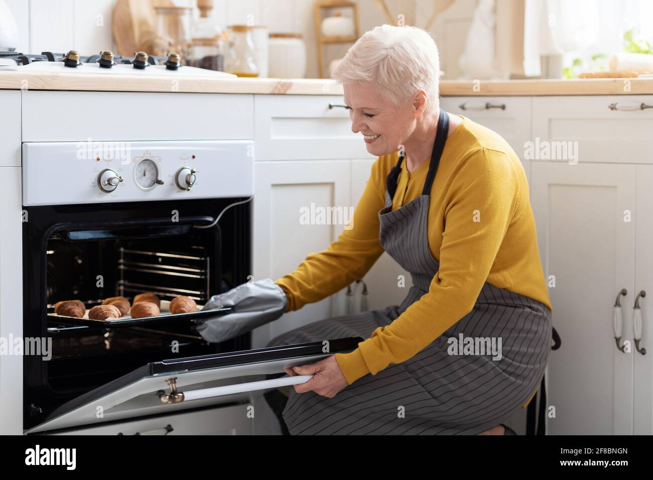 Femme âgée souriante prenant des croissants au four Banque D'Images