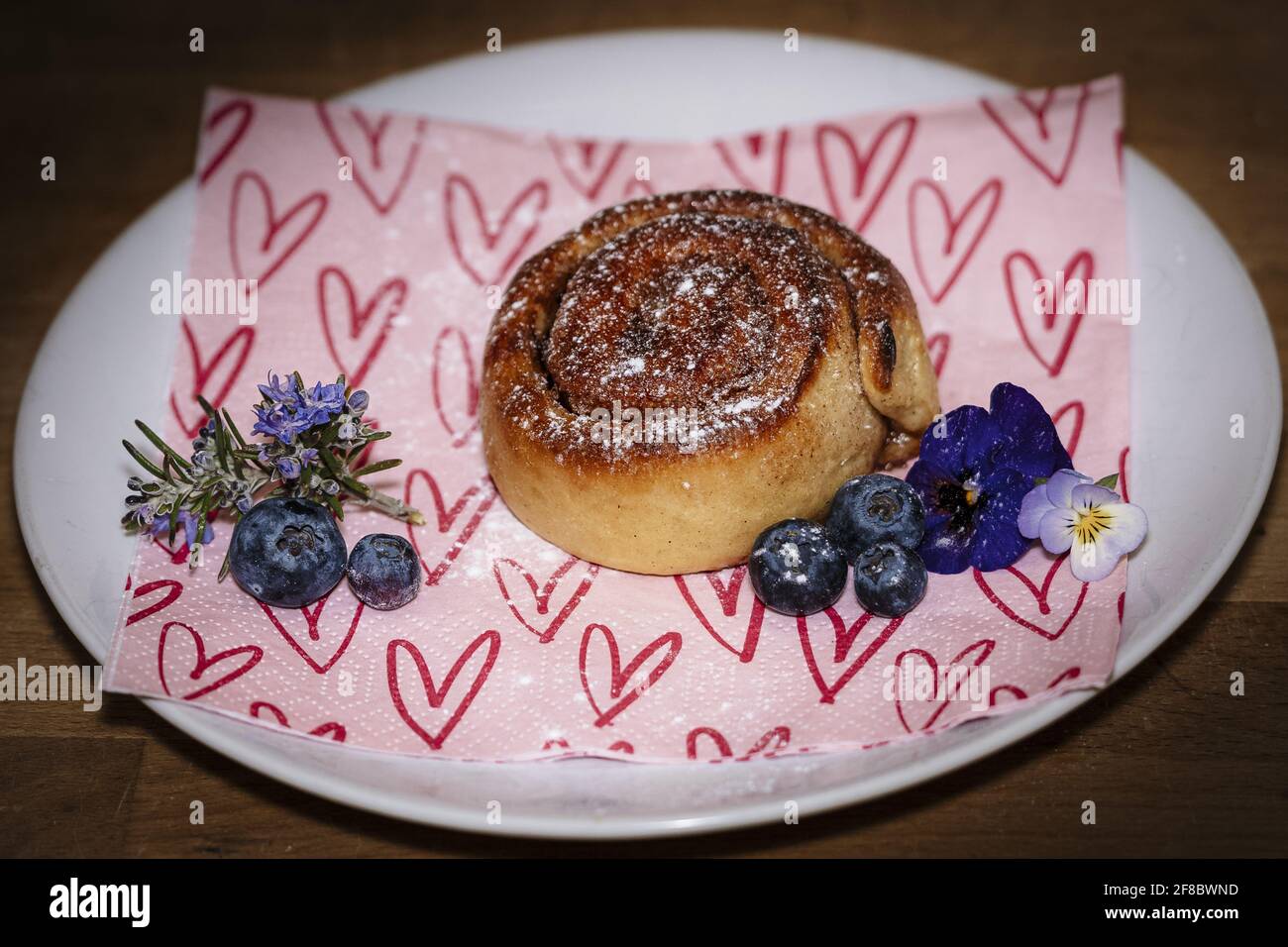 Roulé à la cannelle sur une assiette de bleuets et de fleurs Banque D'Images