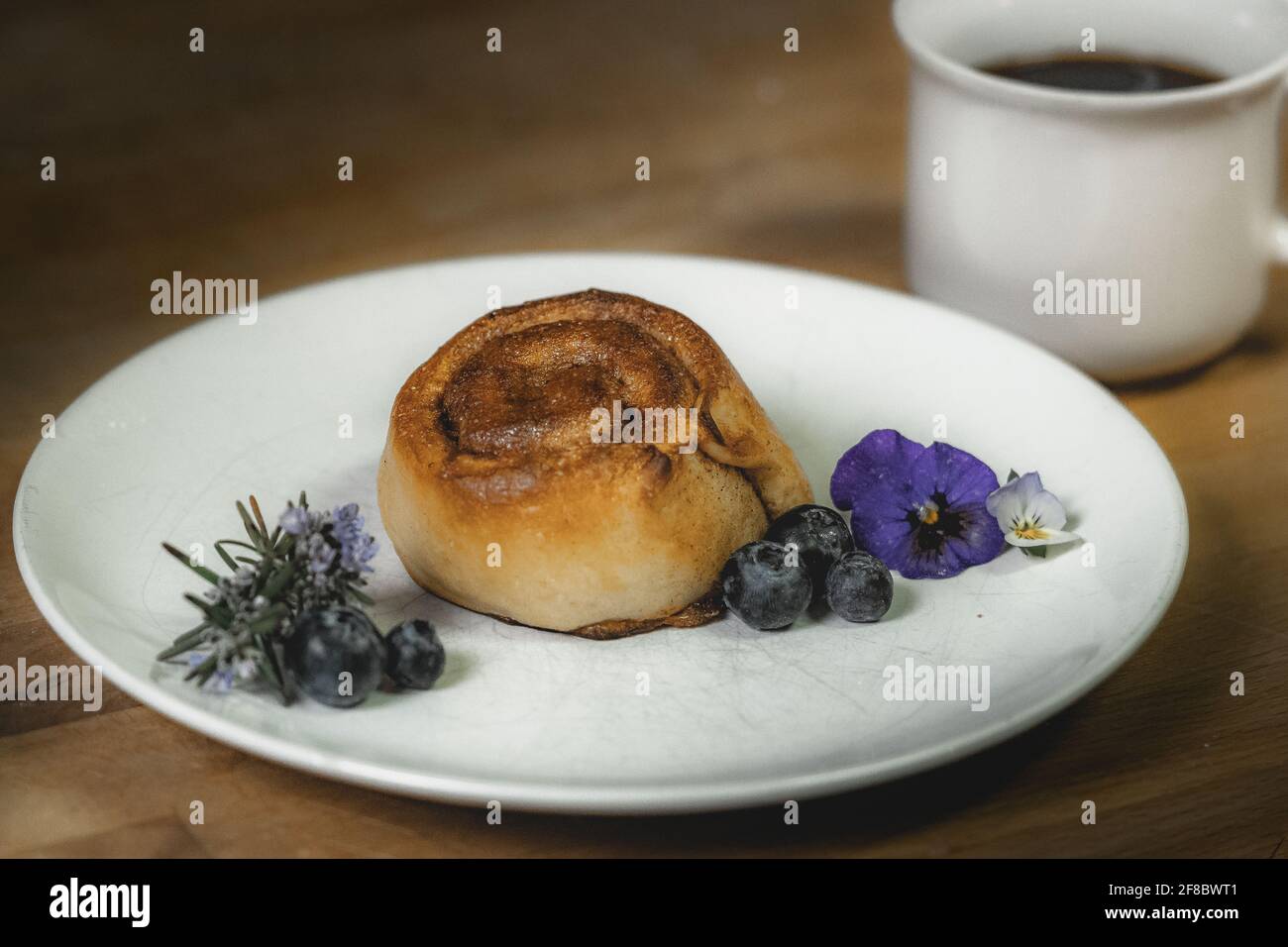 Roulé à la cannelle sur une assiette de bleuets et de fleurs Banque D'Images