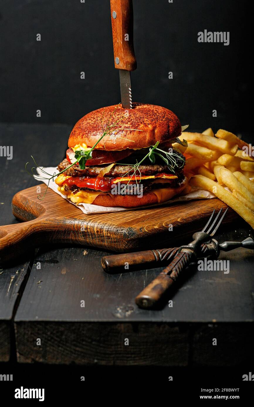 Un hamburger de bœuf double appétissant et une portion de frites sur une planche à découper en bois. Arrière-plan rustique sombre. Photographie de la restauration rapide STILL Life. Sho vertical Banque D'Images