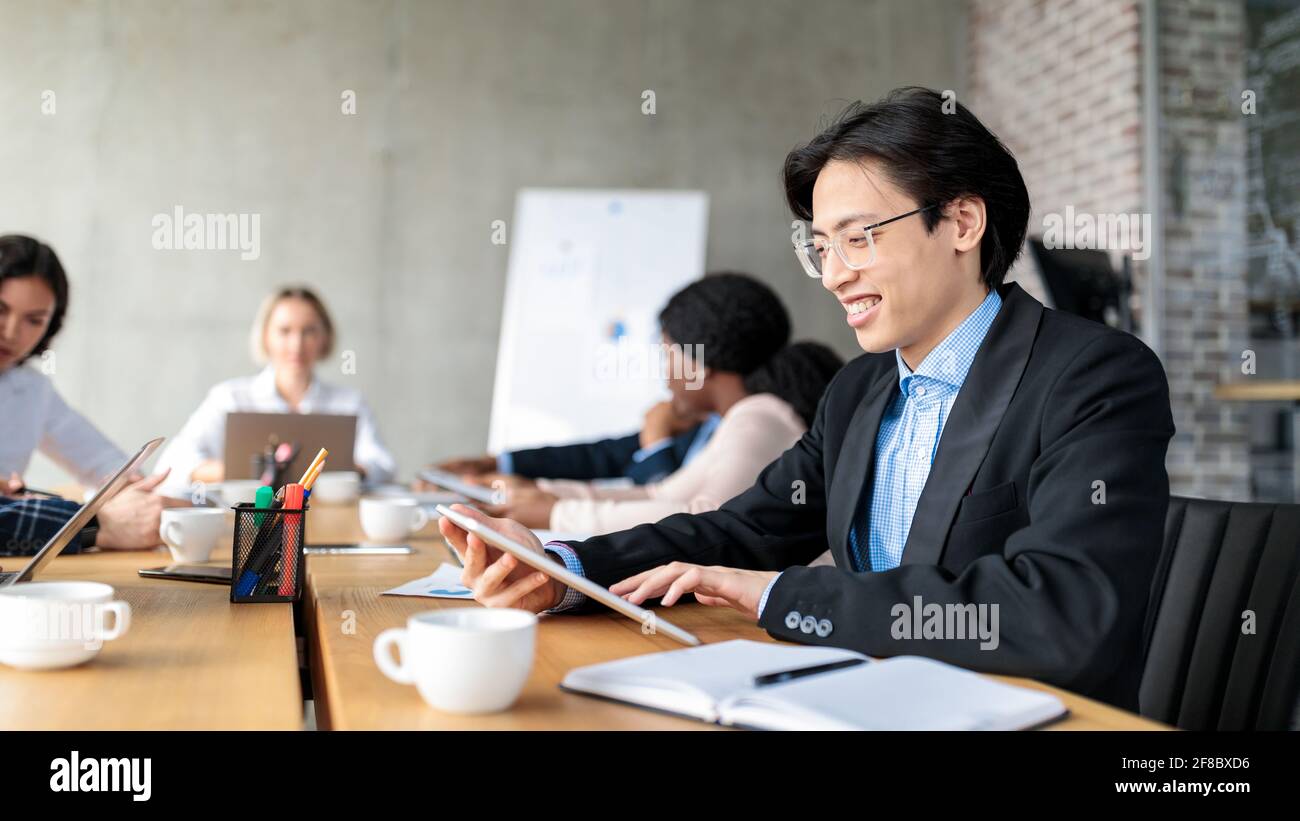 Homme d'affaires japonais utilisant une tablette assis à l'intérieur de réunion d'entreprise, Panorama Banque D'Images
