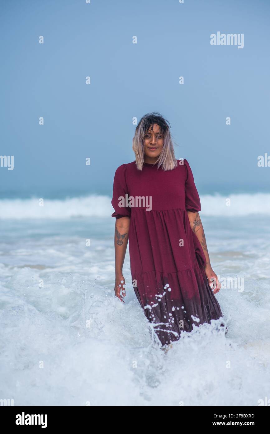Femme debout dans l'eau à la plage avec ses vêtements Banque D'Images