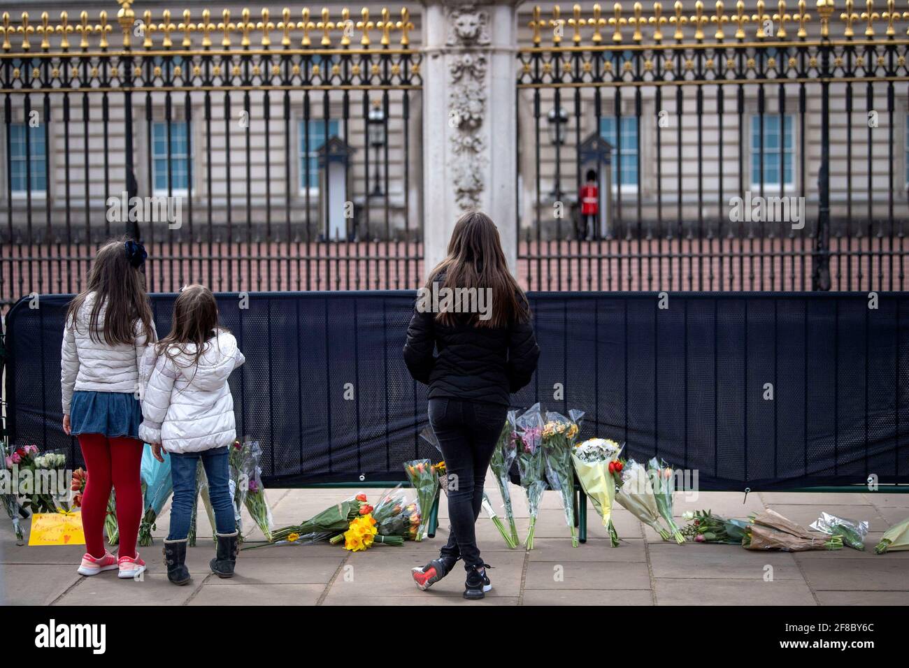 Trois filles regardent des fleurs et des messages laissés par le public à l'extérieur de Buckingham Palace, Londres, après la mort du duc d'Édimbourg à l'âge de 99 ans vendredi. Date de la photo: Mardi 13 avril 2021. Banque D'Images