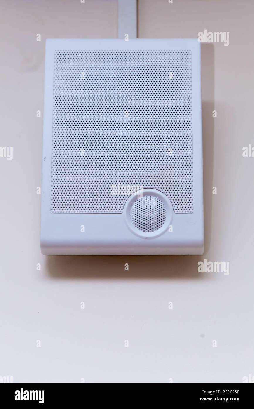 Un émetteur radio blanc est fixé sur un mur beige. Sur la face avant se trouve une grille avec de petits trous pour un haut-parleur. Appareil électronique pour écouter des messages, de la musique et des actualités. Banque D'Images