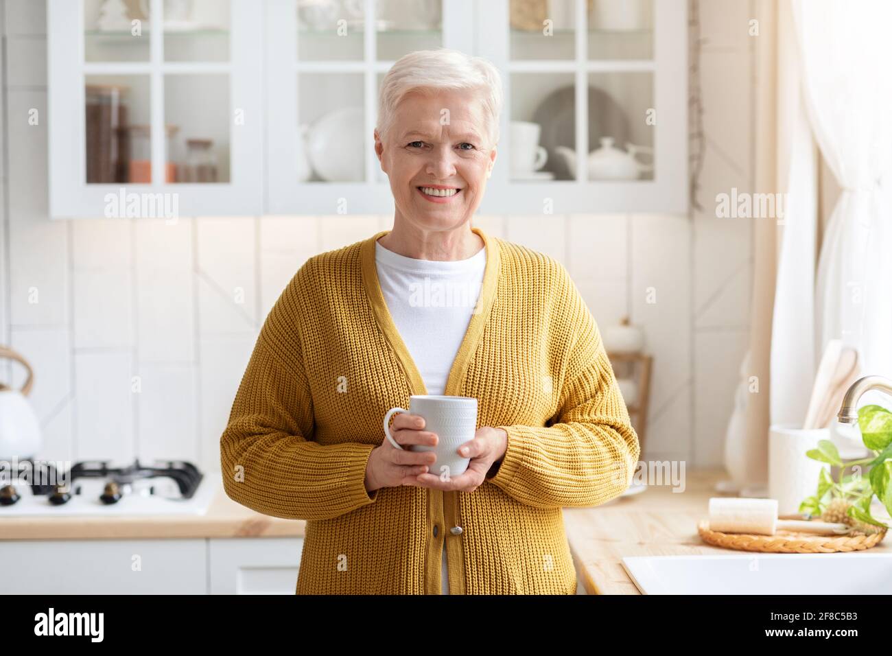 Charmante femme âgée avec tasse, café dans la cuisine Banque D'Images