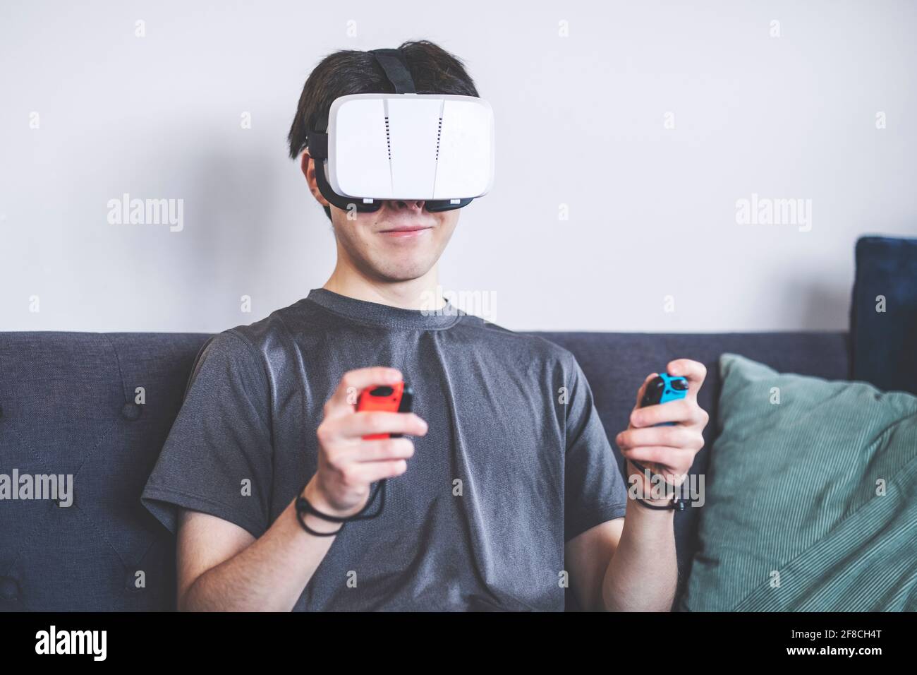 Jeux à la maison avec un casque VR, réalité virtuelle, adolescent / jeune homme dans ses années vingt, décor de salon, assis sur un canapé Banque D'Images