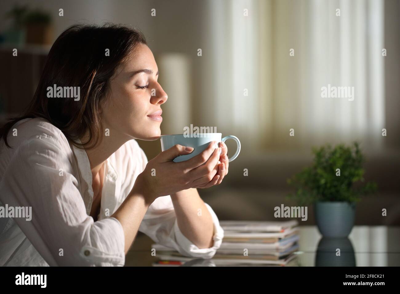 Profil d'une femme détendue qui sent le café la nuit à la maison Banque D'Images