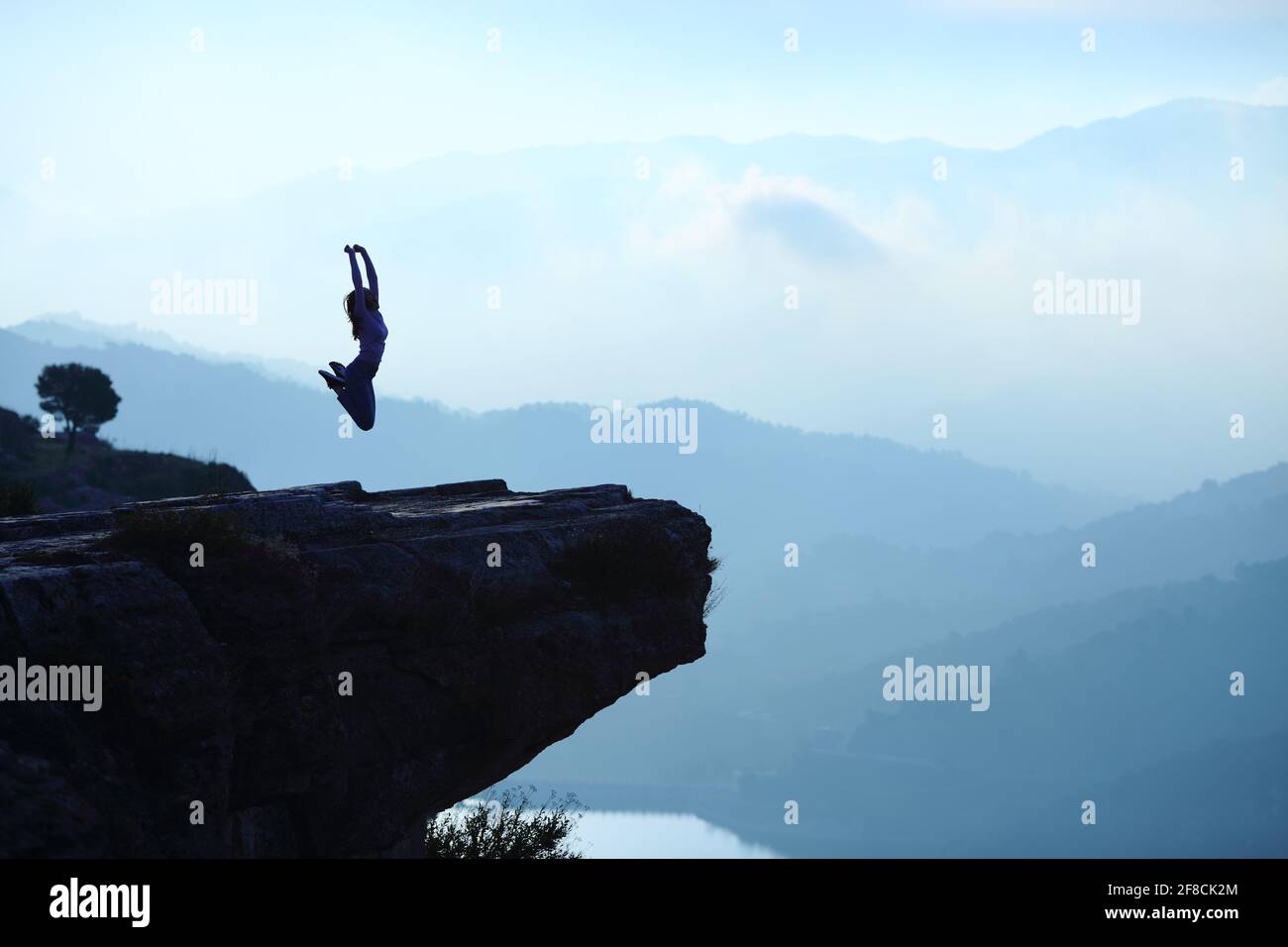 Portrait de contre-jour d'une silhouette de femme sautant en haut d'une falaise sur paysage bleu Banque D'Images