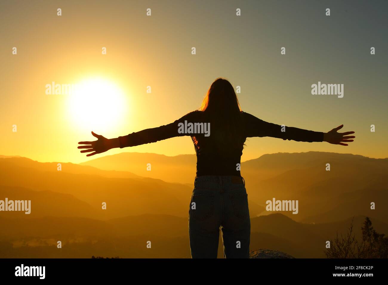 Vue arrière silhuette d'une femme se propageant à bras ouverts au coucher du soleil dans la montagne Banque D'Images