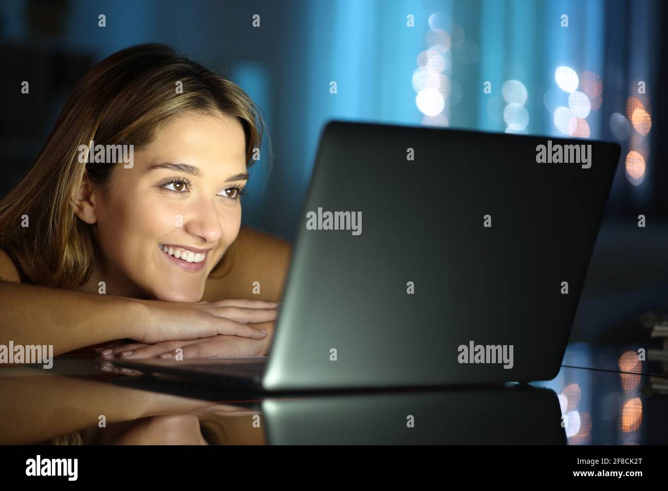 Une femme heureuse souriant à regarder des médias sur un ordinateur portable dans la nuit à la maison Banque D'Images